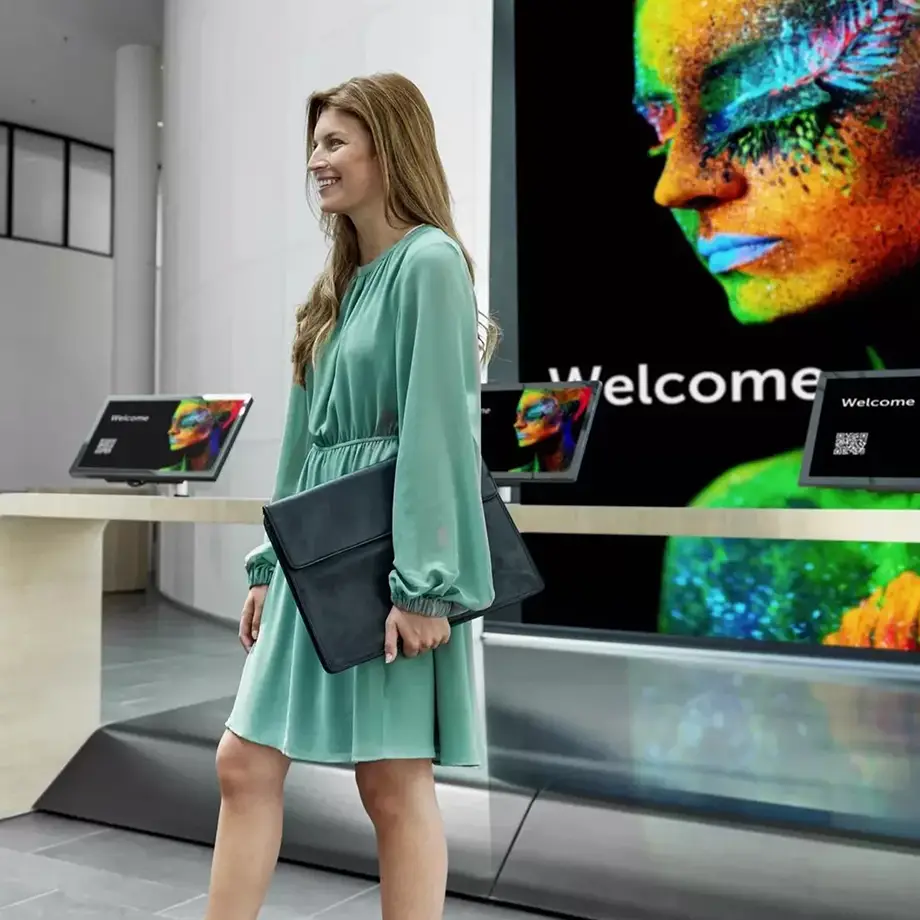 Woman interacting with digital signage and check-in kiosks in modern lobby with welcome display