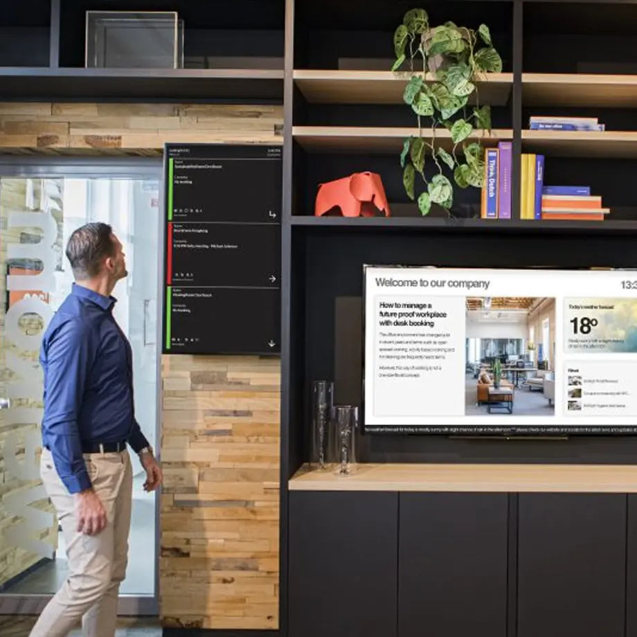 Man viewing digital displays with real-time workplace updates, showcasing AV integration and desk booking technolog